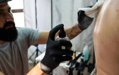 Tattoo artist spraying Calendula onto customers skin