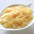 Pale yellow wax flakes in a white leaf-shaped dish on a light wooden surface.