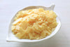 Pale yellow wax flakes in a white leaf-shaped dish on a light wooden surface.