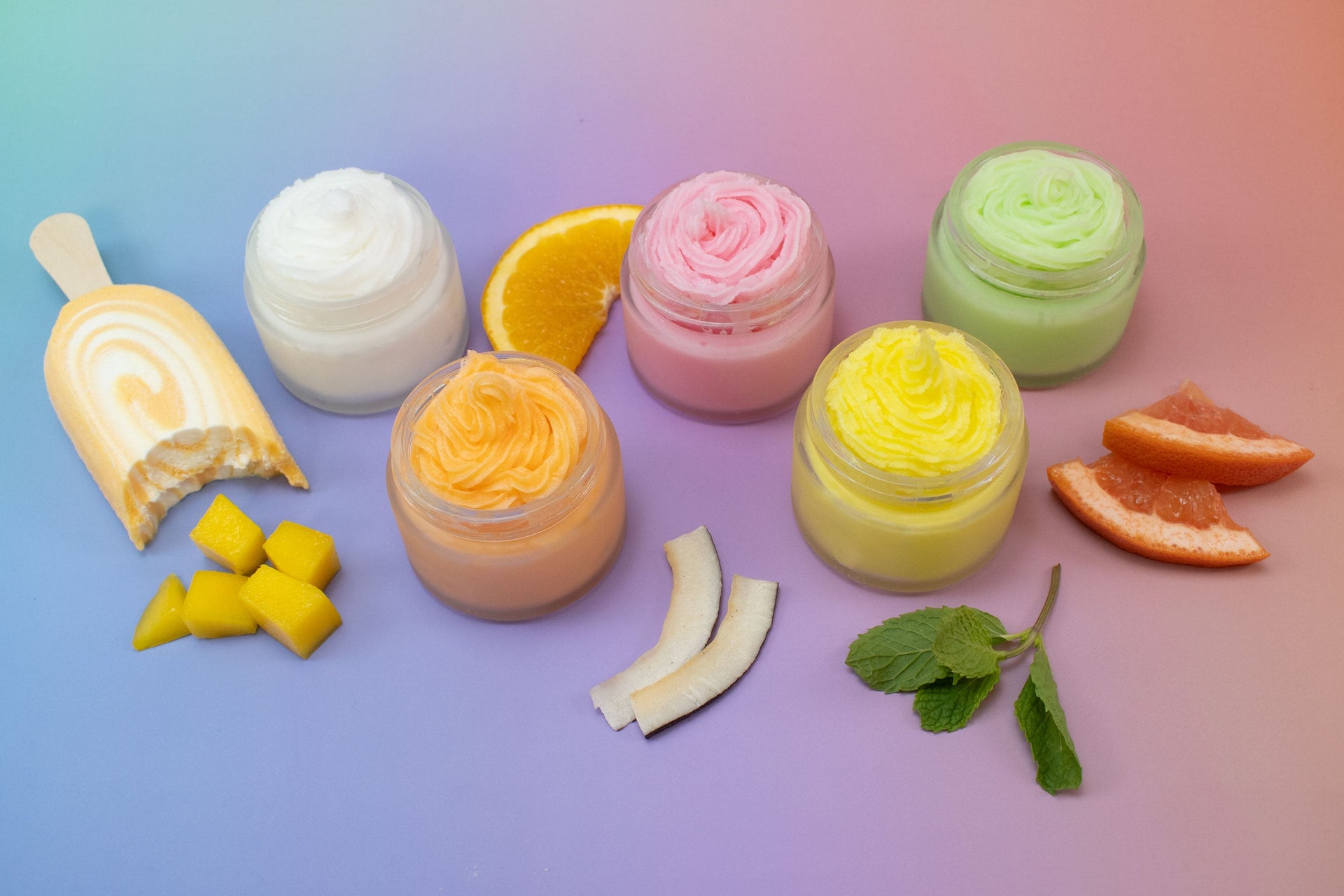 Jars of whipped soap and ingredients spread out over a ombré background