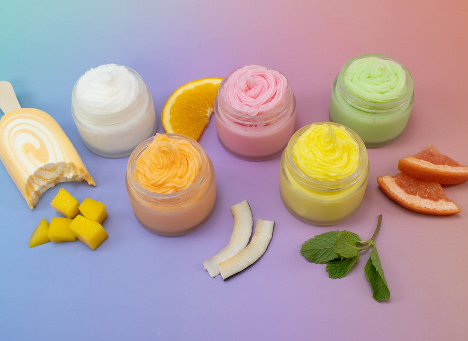 Jars of whipped soap and ingredients spread out over a ombré background