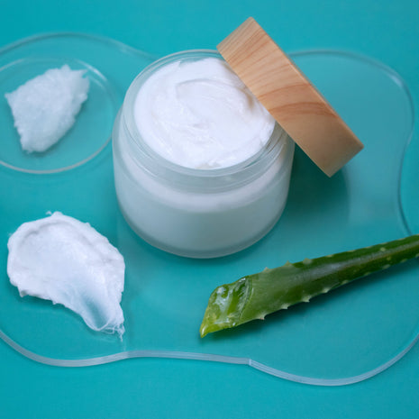 Jar of white cream with aloe vera leaf on a teal background