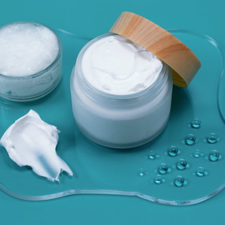 Jar of white cream with a wooden lid on a teal background