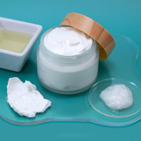 Jar of white cream with a wooden lid on a teal background