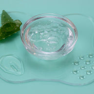Clear gel in a small glass bowl with an aloe vera leaf on a light green background