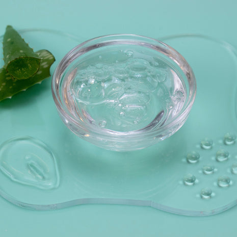 Clear gel in a small glass bowl with an aloe vera leaf on a light green background