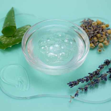 Clear jar of jelly with aloe vera leaves and lavender flowers on a light green background