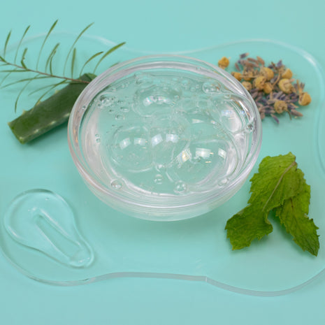 Clear jar of skincare product with aloe vera, lavender, and mint leaves on a light blue background
