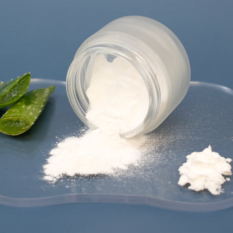 White powder spilling out of a glass jar on a blue surface with aloe leaves.