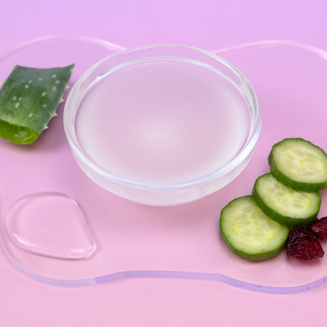 Clear gel in a bowl with aloe vera leaf, cucumber slices, and berries on a pink background