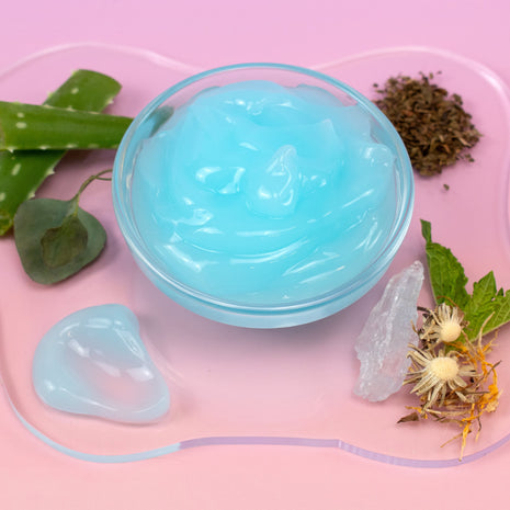 Arctic Blue Cooling Gel in a container with aloe vera leaves and herbs on a pink background