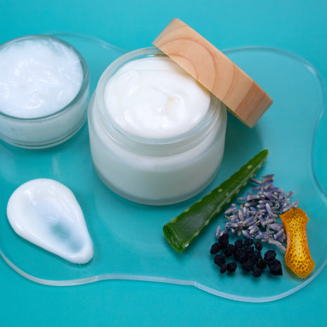Jar of AHA Aftershave Lotion with a wooden applicator on a blue background with natural ingredients.
