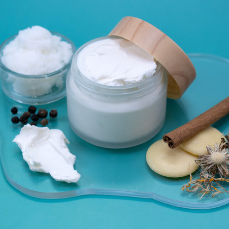 Cocoa & Shea Soothing Muscle Lotion with a wooden lid on a blue background.