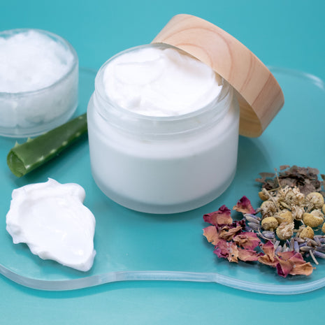 Jar of Herbal Lotion with wooden lid on a blue background with dried flowers and aloe vera.
