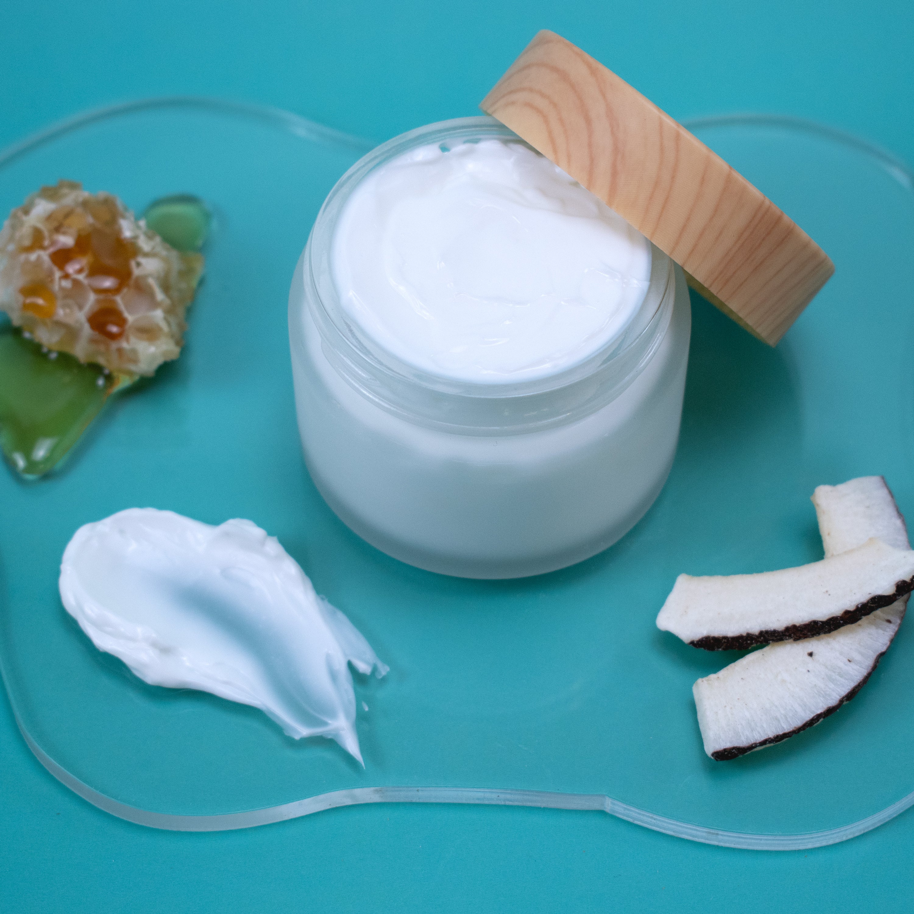 Jar of Milk & Honey Lotion with a wooden lid on a blue background with coconut pieces and honeycomb.