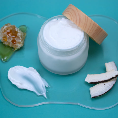 Jar of Milk & Honey Lotion with a wooden lid on a blue background with coconut pieces and honeycomb.
