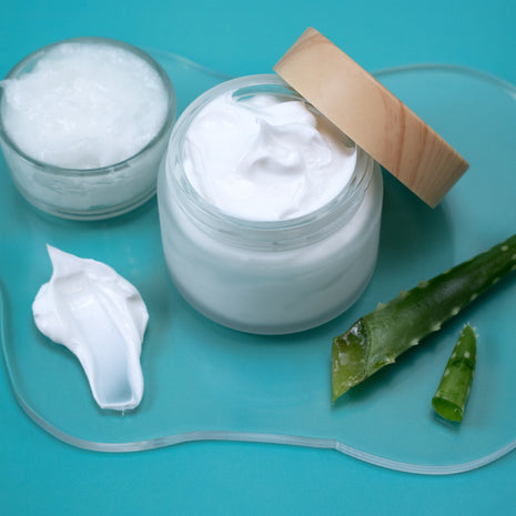 Jar of Simple Lotion with aloe vera leaves on a blue background