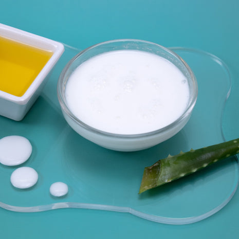 Bowl of Jojoba Spray Lotion with aloe vera leaf and jojoba oil on a teal background