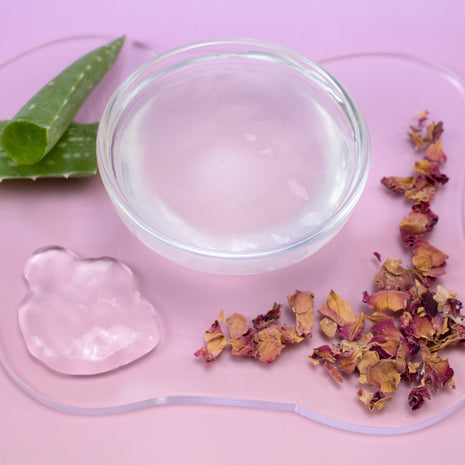 Bowl with Glycolic & Rose Gel Mask, aloe vera leaves, and dried flowers on a pink background