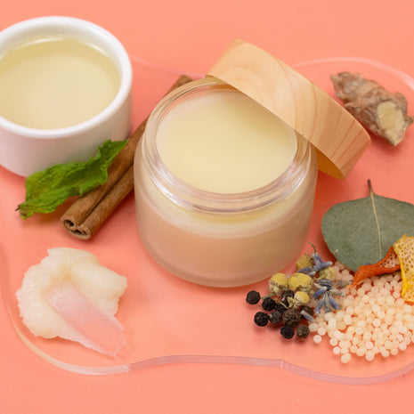 Jar of Body Balm with wooden lid on a pink background with natural ingredients