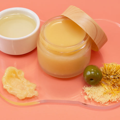 Jar of Vegan Diaper Balm with a wooden lid on a pink background