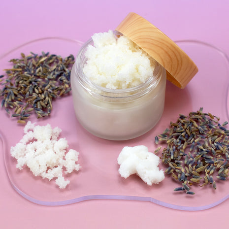 Jar of Lavender Shortbread Cookie Scrub with a wooden lid on a pink tray with lavender flowers