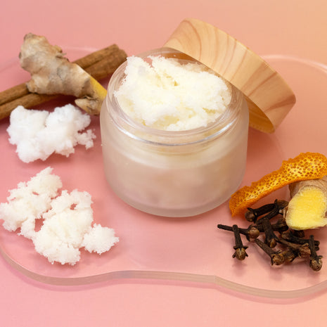Jar of Gingerbread Sugar Scrub with wooden lid on a pink background with natural ingredients