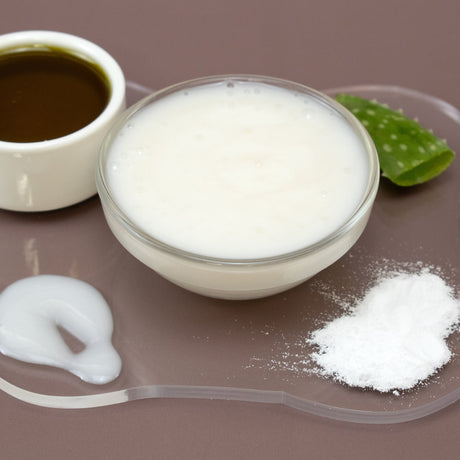 Glass bowl with Niacinamide Facial Serum, aloe vera leaf, and other ingredients on a brown background