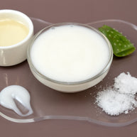 Glass bowl of DMAE & MSM Facial Serum with aloe vera leaf and leaves on a brown background