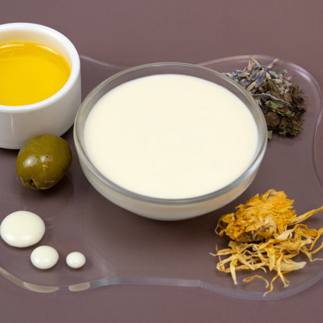 Bowl of Equalizer Facial Serum with oil, green olive, and dried herbs on a purple surface