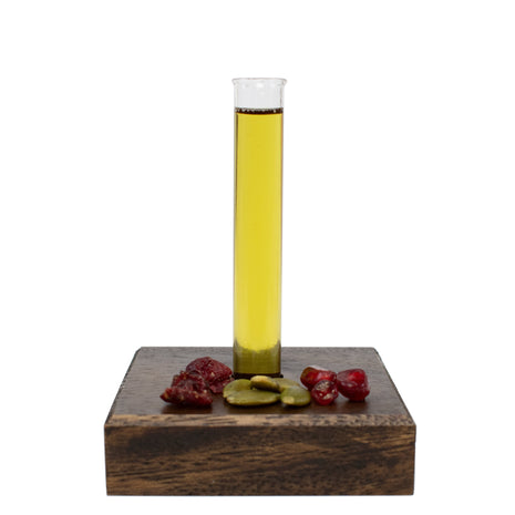 Glass tube with Exquisite Face, Hair, & Body Oil on a wooden block with fruit pieces against a white background