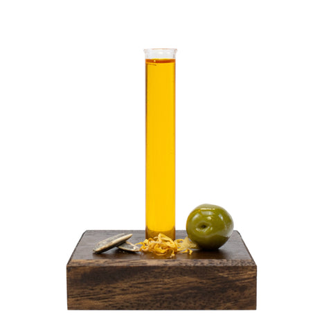 Glass beaker with Every Body Oil on a wooden block with an olive and natural ingredients.