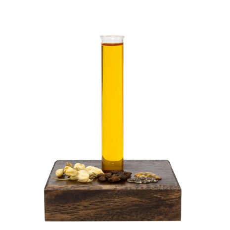 Beaker with Rejuvenating Skin Oil on a wooden block with dried herbs, against a white background