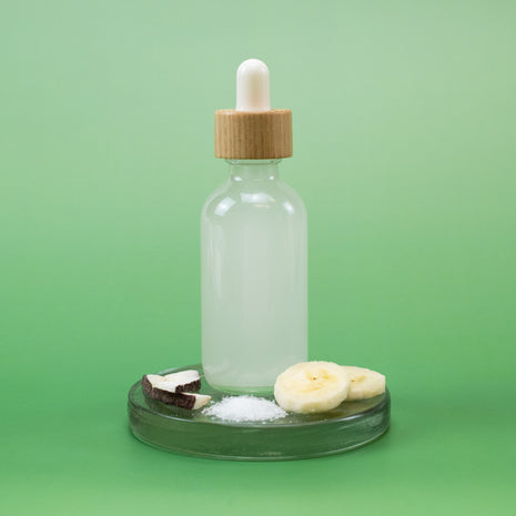 Clear glass bottle with MSM Rejuvenating Facial Toner in wooden dropper bottle with natural ingredients on a green background