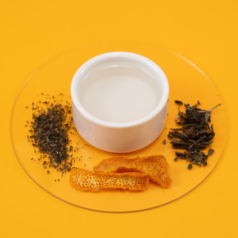 White bowl with Refreshing Body Spritz, tea leaves and dried fruit on a yellow background