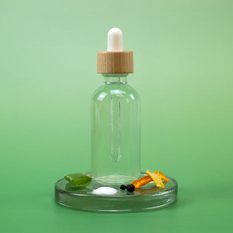 AHA Facial Toner in a clear glass dropper bottle with wooden cap on a green background