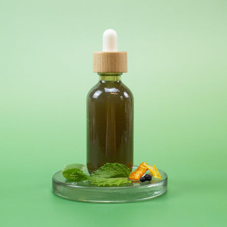 Bottle of Peppermint Facial Toner with a dropper and natural ingredients on a green background