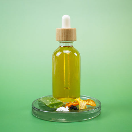 Vitamin C Facial Toner in a bottle with a dropper on a clear stand with natural ingredients against a green background