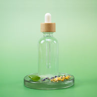 Herbal Tea Facial Toner in a clear glass dropper bottle with wooden cap and natural ingredients on a green background