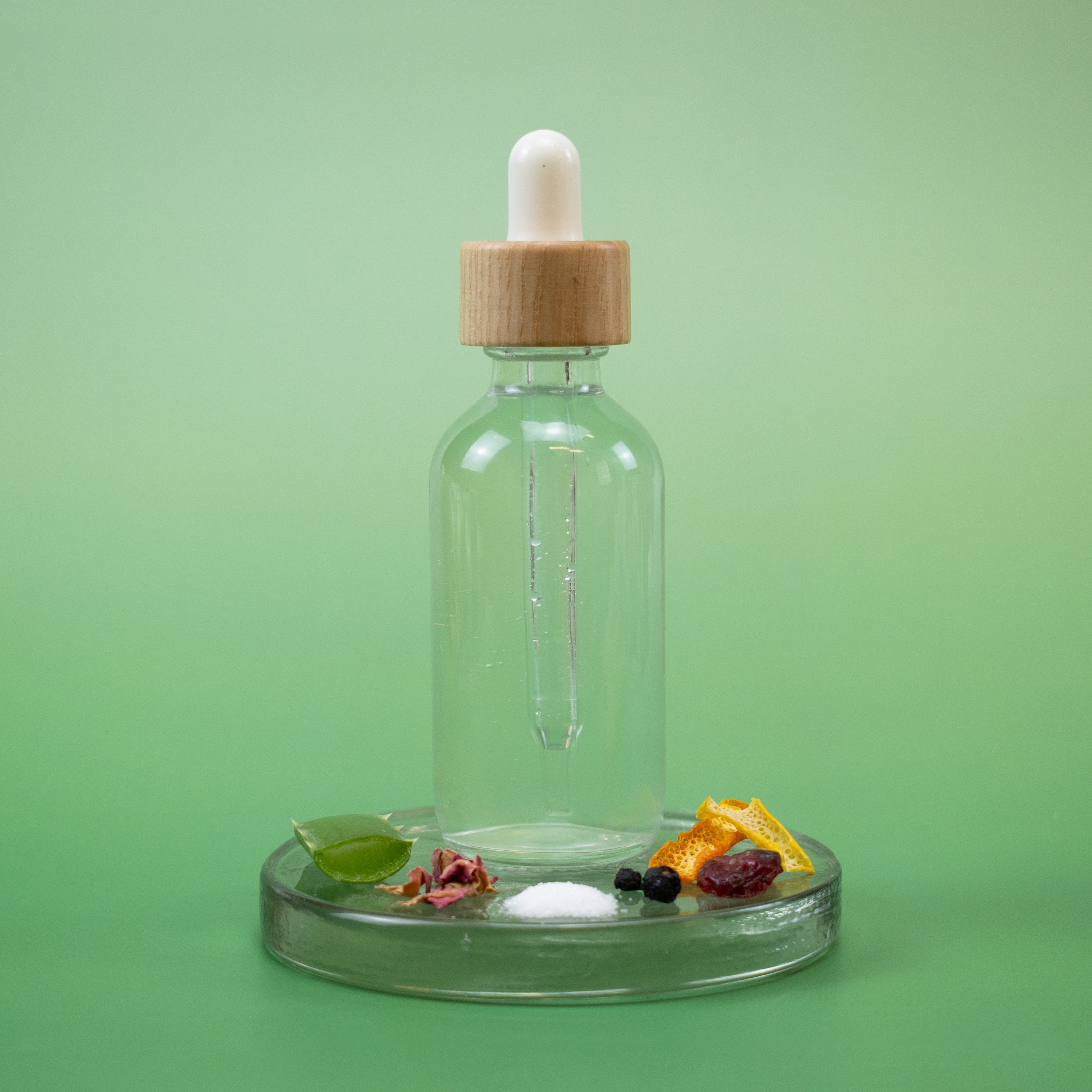 Mature Skin Facial Toner in a clear glass dropper bottle with wooden cap and natural ingredients on a green background