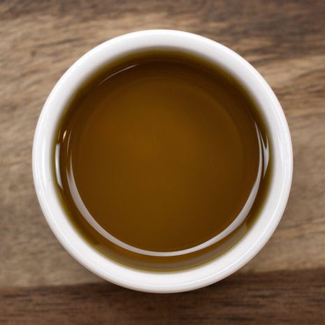 White bowl filled with Carrot Seed Oil on a wooden surface