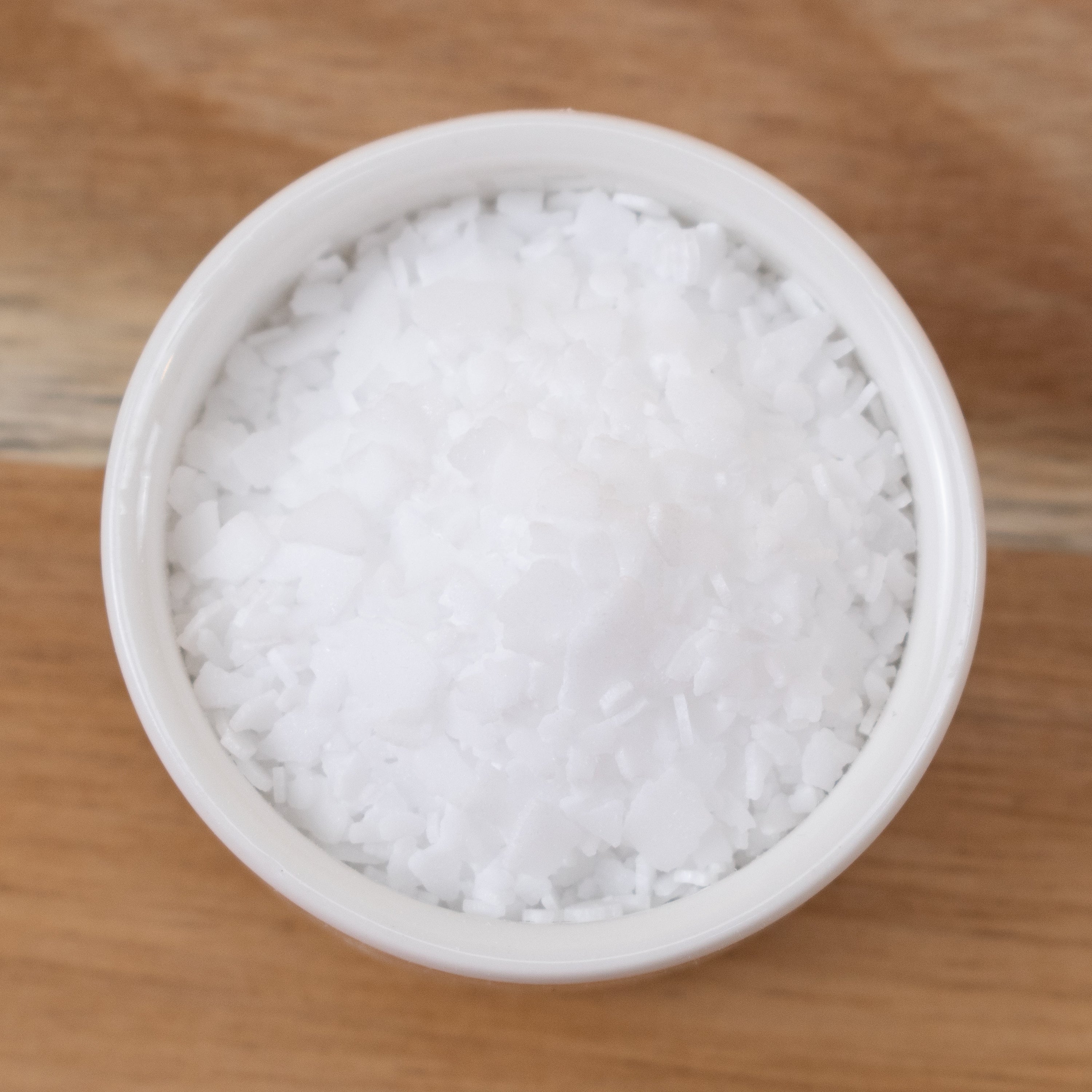 Stearic Acid in a small white container on a wooden surface