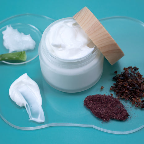 Jar of Rosehip & Hibiscus Facial Lotion with a wooden lid on a blue background